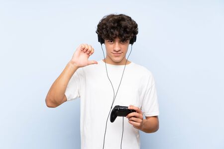 Young man playing with a video game controller over isolated blue wall proud and self-satisfiedの写真素材