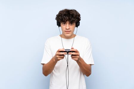 Young man playing with a video game controller over isolated blue wallの写真素材