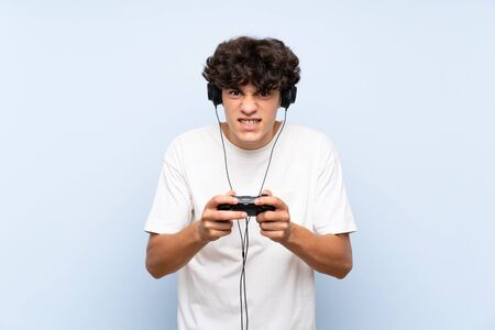 Young man playing with a video game controller over isolated blue wallの写真素材