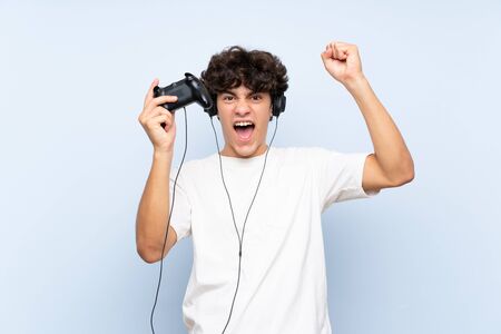 Young man playing with a video game controller over isolated blue wallの写真素材