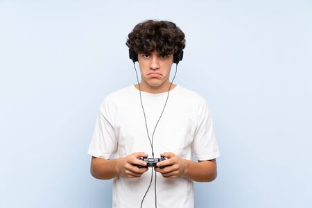 Young man playing with a video game controller over isolated blue wallの写真素材