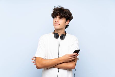 Young man listening music with a mobile over isolated blue wall looking up while smilingの写真素材