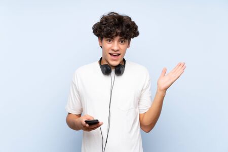 Young man listening music with a mobile over isolated blue wall with shocked facial expressionの写真素材