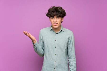Young man over isolated purple wall making doubts gestureの写真素材