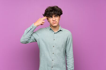 Young man over isolated purple wall with problems making suicide gestureの写真素材