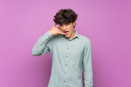 Young man over isolated purple wall making phone gesture. Call me back signの写真素材
