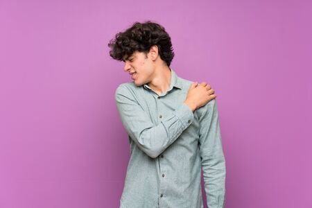 Young man over isolated purple wall suffering from pain in shoulder for having made an effortの写真素材