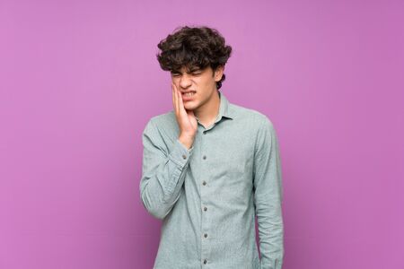 Young man over isolated purple wall with toothacheの写真素材