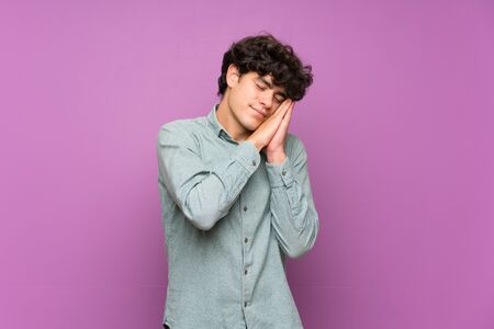 Young man over isolated purple wall making sleep gesture in dorable expressionの写真素材