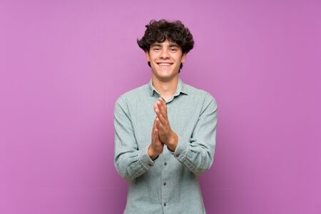 Young man over isolated purple wall applauding after presentation in a conferenceの写真素材