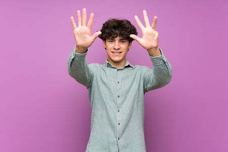 Young man over isolated purple wall counting nine with fingersの写真素材