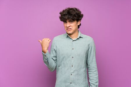 Young man over isolated purple wall unhappy and pointing to the sideの写真素材