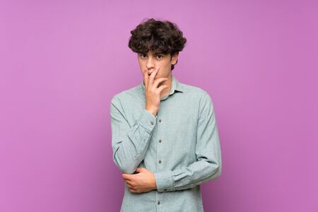 Young man over isolated purple wall surprised and shocked while looking rightの写真素材