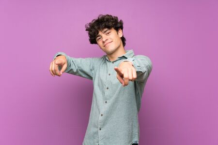 Young man over isolated purple wall points finger at you while smilingの写真素材