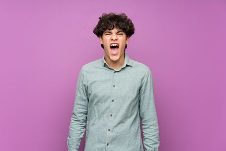 Young man over isolated purple wall shouting to the front with mouth wide openの写真素材