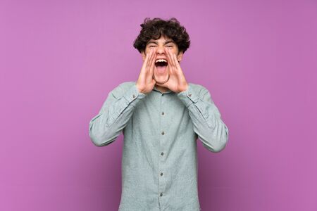 Young man over isolated purple wall shouting and announcing somethingの写真素材
