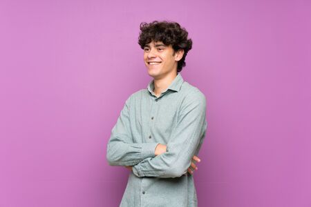 Young man over isolated purple wall with arms crossed and looking forwardの写真素材