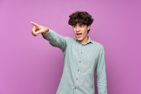 Young man over isolated purple wall pointing awayの写真素材