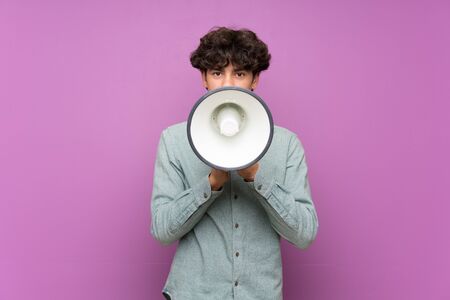 Young man over isolated purple wall shouting through a megaphoneの写真素材