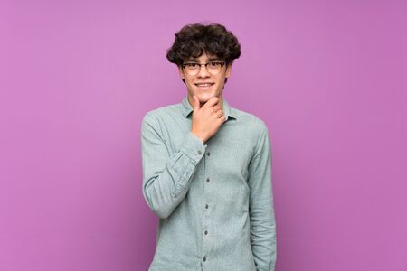 Young man over isolated purple wall with glasses and smilingの写真素材