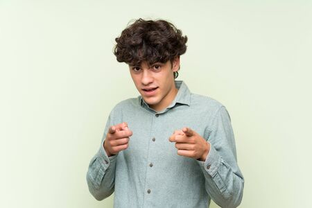 Young man over isolated green wall points finger at youの写真素材