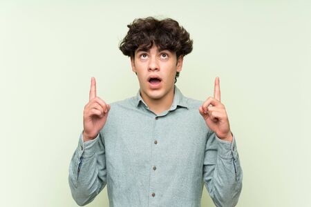 Young man over isolated green wall pointing with the index finger a great ideaの写真素材