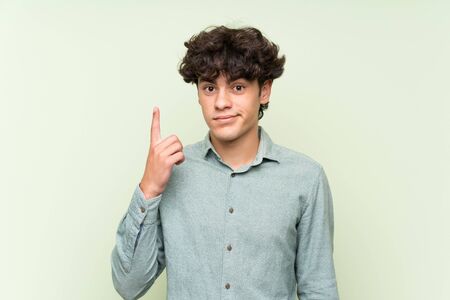 Young man over isolated green wall pointing with the index finger a great ideaの写真素材