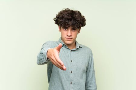 Young man over isolated green wall handshaking after good dealの写真素材