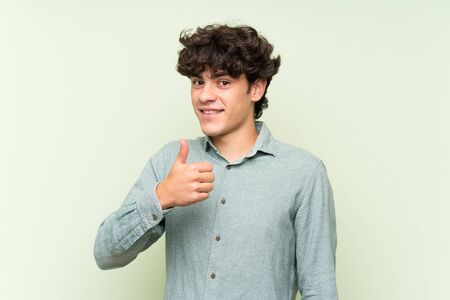 Young man over isolated green wall giving a thumbs up gestureの写真素材