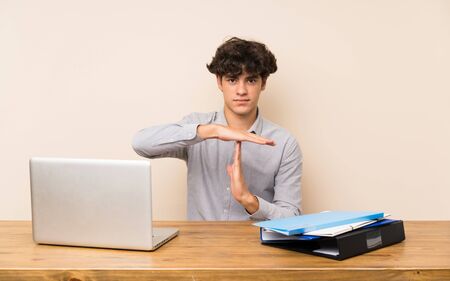 Young student man with a laptop making time out gestureの写真素材