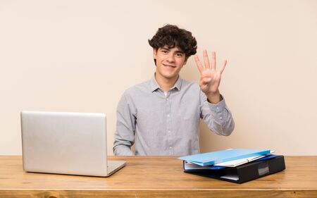 Young student man with a laptop happy and counting four with fingersの写真素材