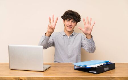 Young student man with a laptop counting eight with fingersの写真素材