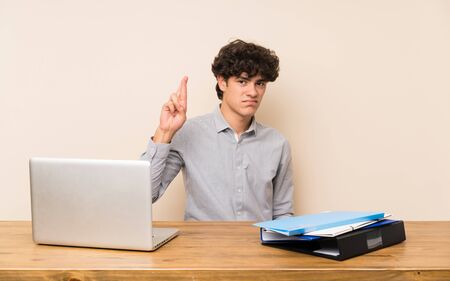 Young student man with a laptop with fingers crossing and wishing the bestの写真素材