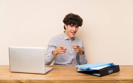 Young student man with a laptop pointing to the front and smilingの写真素材