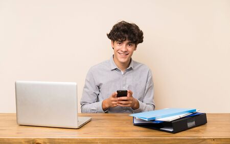 Young student man with a laptop sending a message with the mobileの写真素材