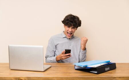 Young student man with a laptop with phone in victory positionの写真素材