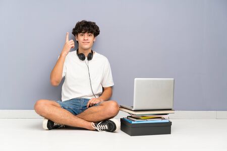 Young man with his laptop sitting one the floor pointing with the index finger a great ideaの写真素材