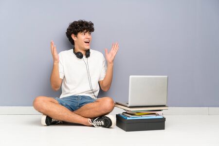 Young man with his laptop sitting one the floor with surprise facial expressionの写真素材