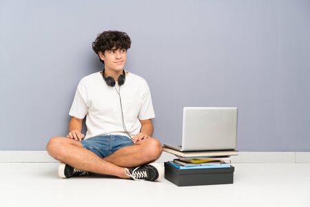 Young man with his laptop sitting one the floor standing and looking to the sideの写真素材