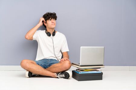 Young man with his laptop sitting one the floor having doubts and with confuse face expressionの写真素材