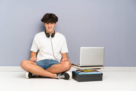 Young man with his laptop sitting one the floor having doubts and with confuse face expressionの写真素材