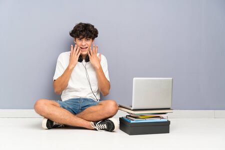 Young man with his laptop sitting one the floor with surprise facial expressionの写真素材