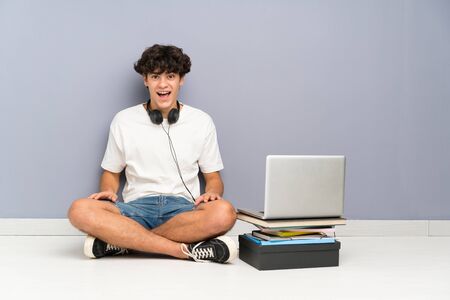 Young man with his laptop sitting one the floor with surprise facial expressionの写真素材