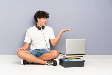 Young man with his laptop sitting one the floor holding copyspace imaginary on the palmの写真素材