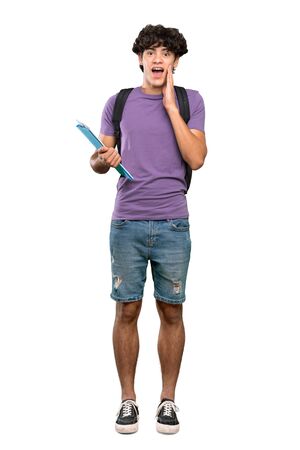 A full-length shot of a Young student man with surprise and shocked facial expression over isolated white backgroundの写真素材