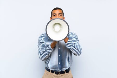Young handsome brunette man over isolated blue background shouting through a megaphoneの写真素材