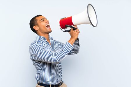 Young handsome brunette man over isolated blue background shouting through a megaphoneの写真素材