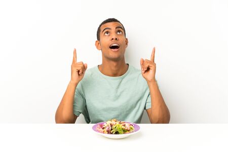 Young handsome man with salad in a table pointing with the index finger a great ideaの写真素材