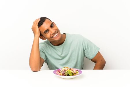 Young handsome man with salad in a table laughingの写真素材
