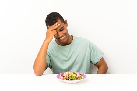 Young handsome man with salad in a table laughingの写真素材